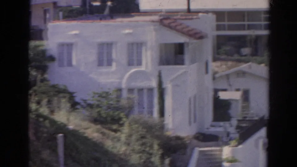 Soft 1966 Silver Lake 8mm frame showing the white stucco house, arched front window, hillside brush, steps, and neighboring residential forms.