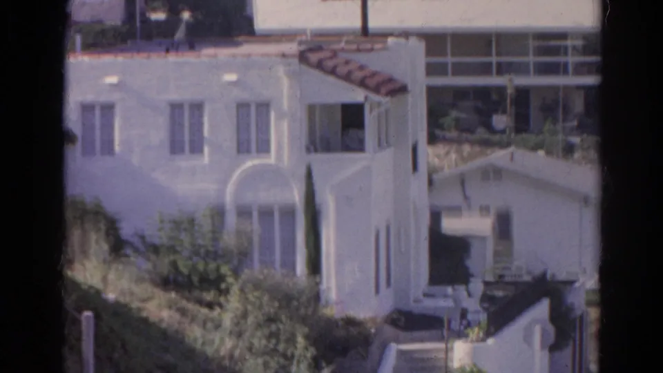 1966 Silver Lake frame showing the white hillside house with arched window, vertical windows, greenery, stairs, and surrounding residential buildings.