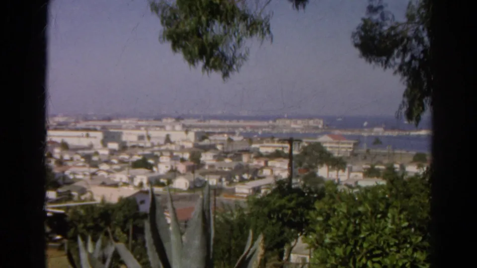 1966 Silver Lake, California home-movie frame showing a distant city and harbor through hillside trees and agave.