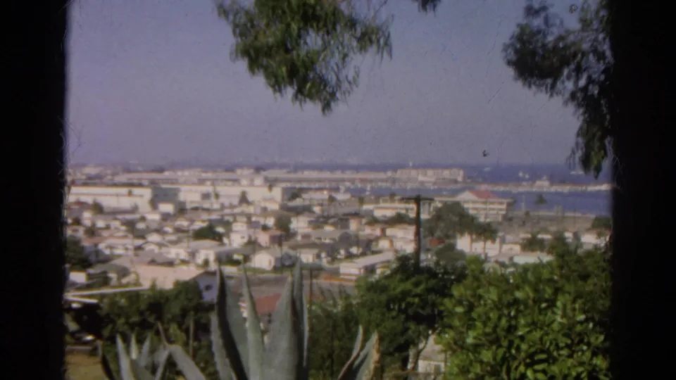 1966 Silver Lake, California home-movie still showing hillside foliage, a large agave, rooftops, and harbor water in the distance.