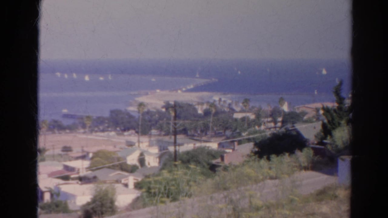 1966 8mm home-movie frame identified as Silver Lake, California, showing an elevated coastal view with sailboats, palms, beach, and hillside homes.