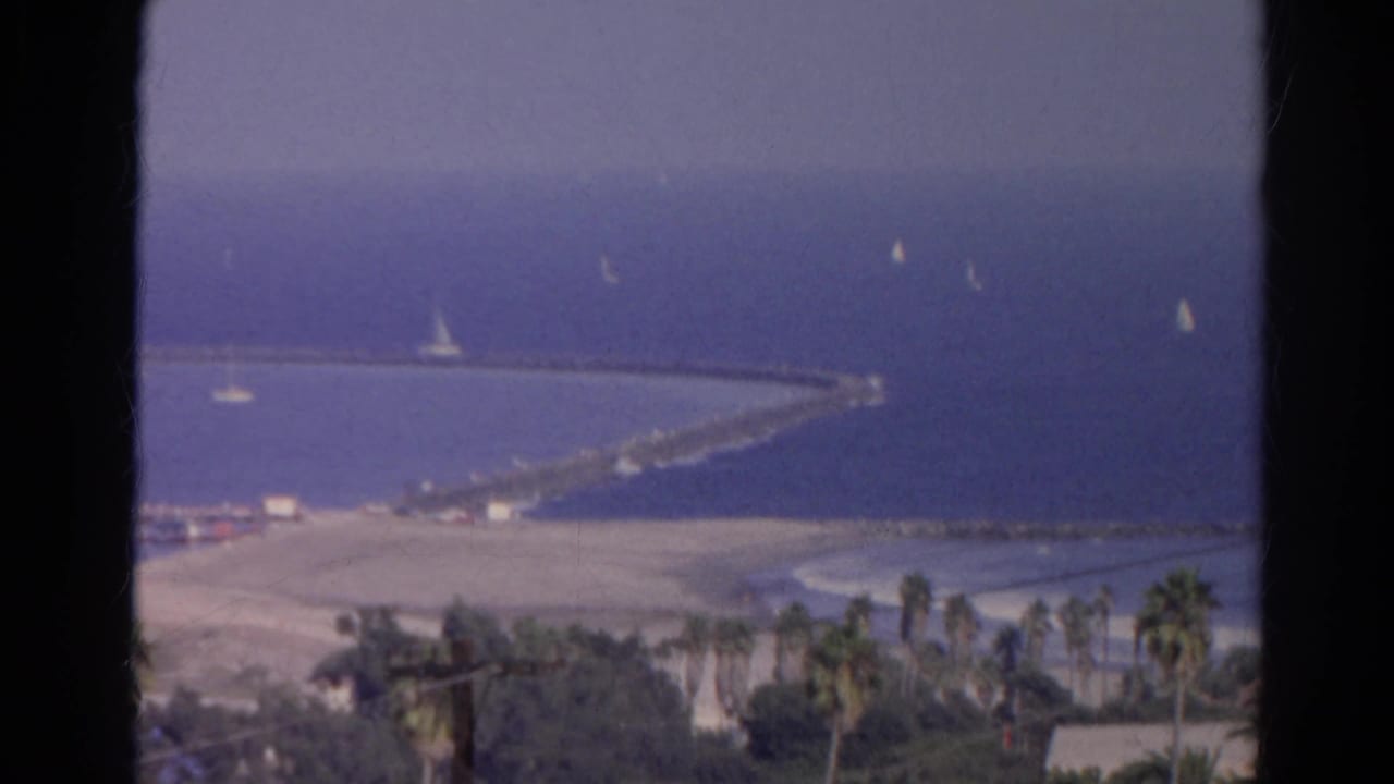 1966 8mm home-movie view identified as Silver Lake, California, showing sailboats near a long pier or breakwater and palm-lined shore.