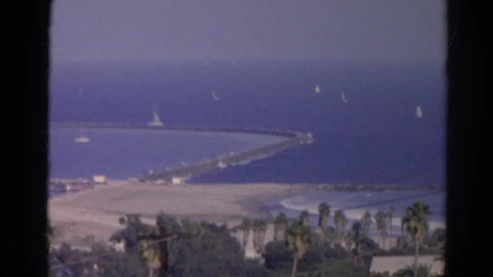 1966 8mm home-movie view identified as Silver Lake, California, showing sailboats near a long pier or breakwater and palm-lined shore.