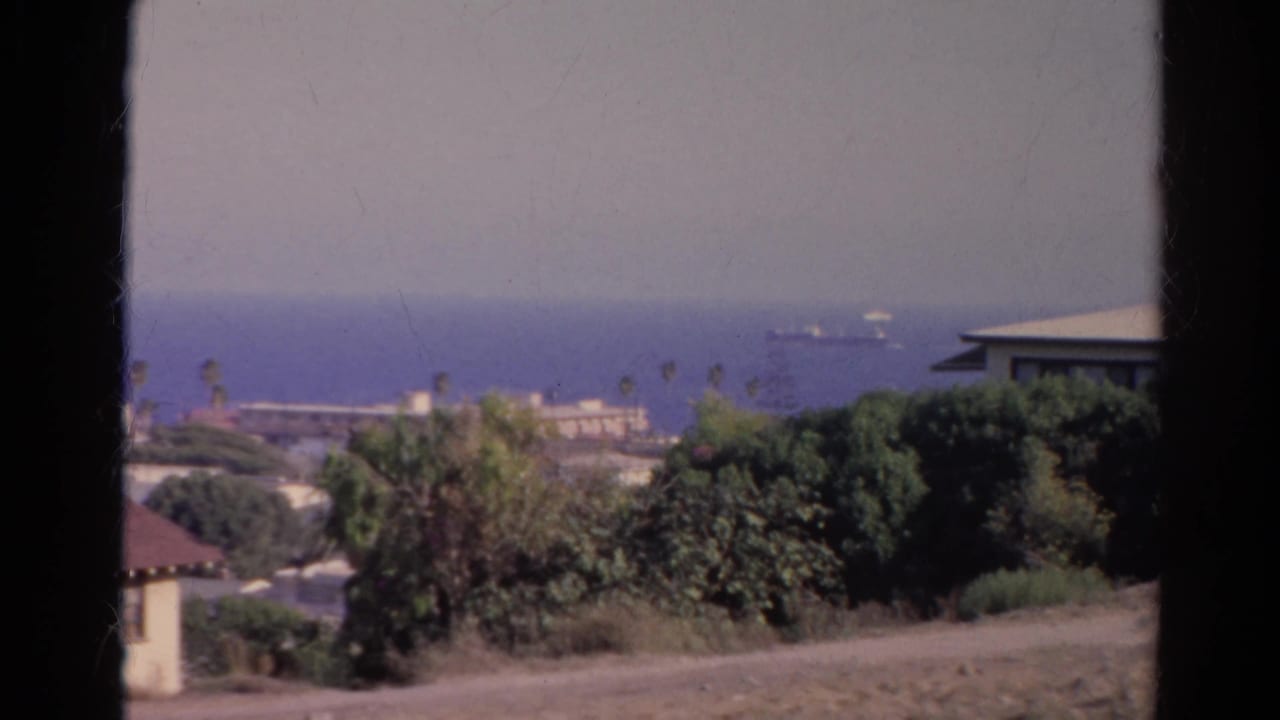1966 California 8mm view of a hazy ocean horizon with ships offshore, hillside vegetation, rooftops, and dark foreground framing.