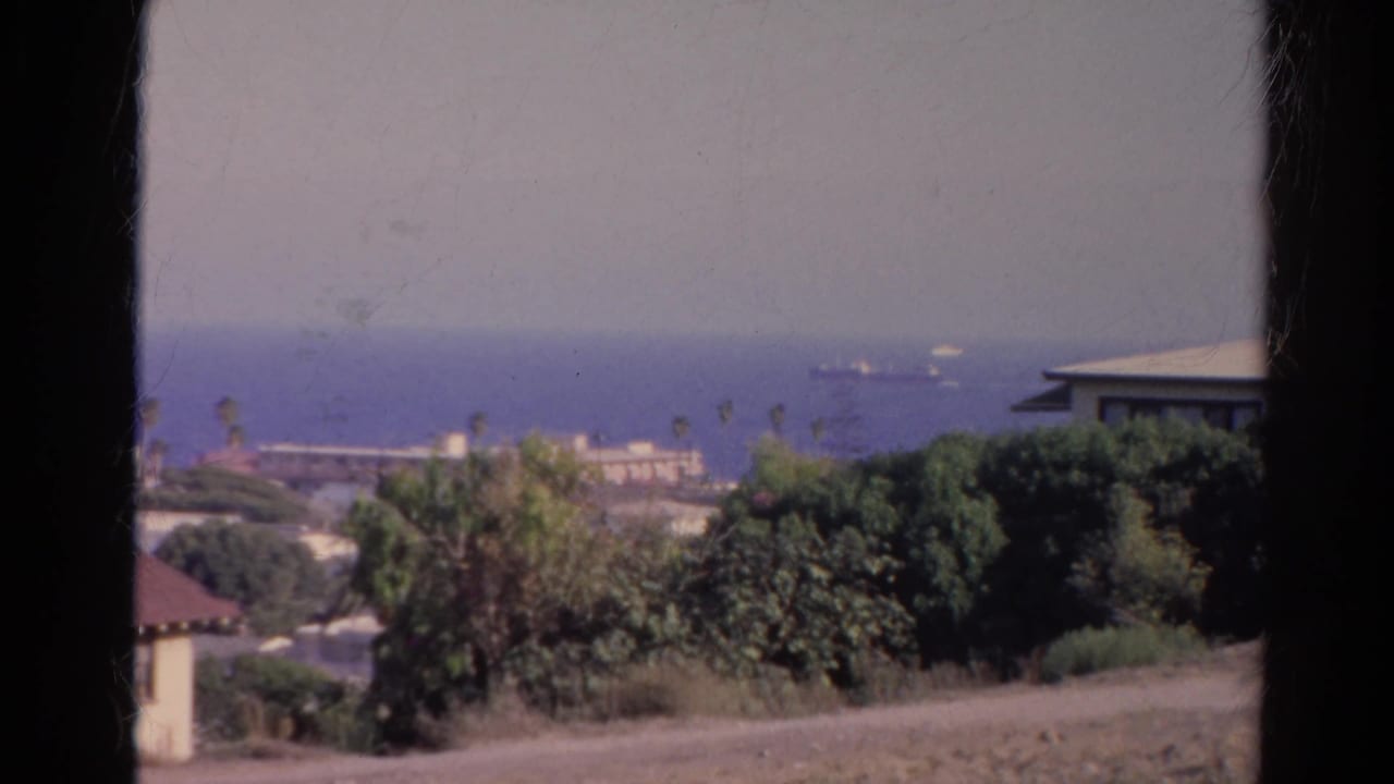 1966 8mm home-movie view of a California coastal overlook with palm trees, low buildings, ocean, and a distant ship.