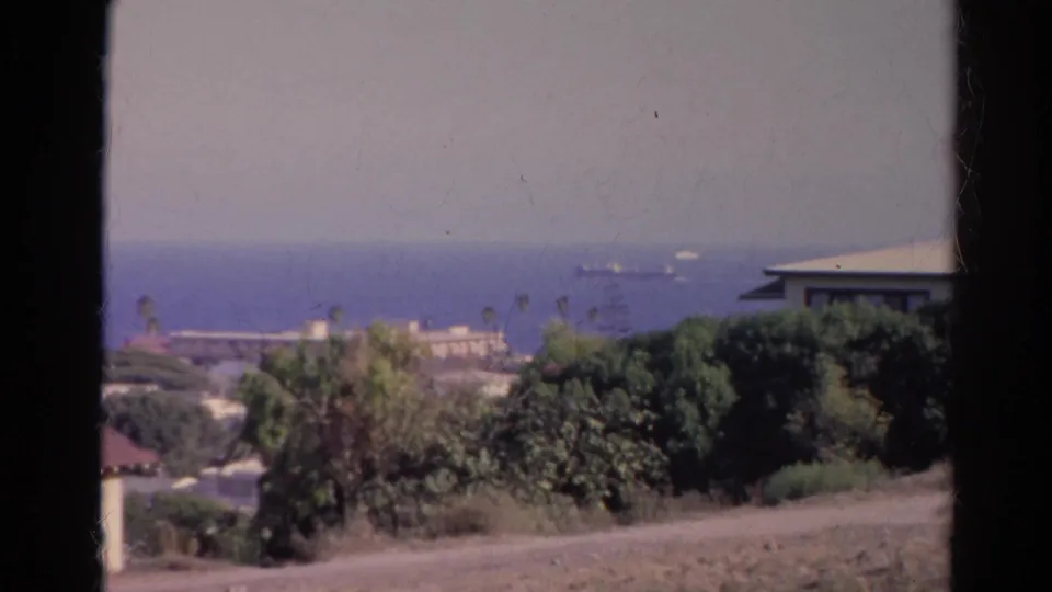 1966 California coastal view from a shaded opening, showing trees, low buildings, ocean horizon, and distant vessels.