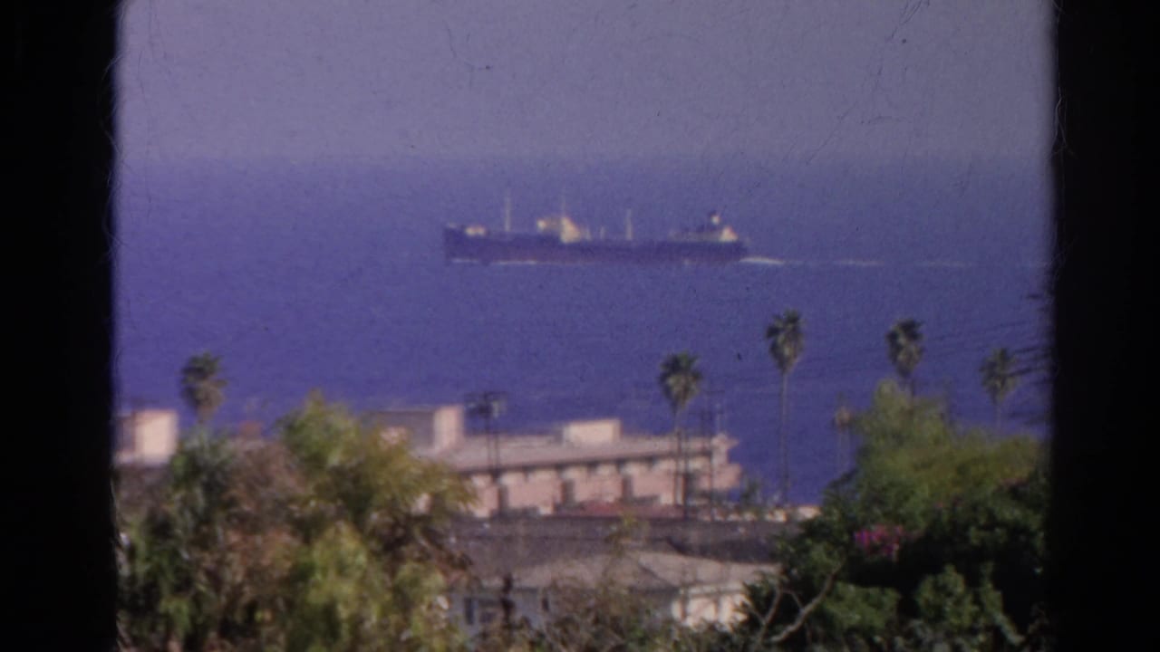 1966 Silver Lake, California 8mm view toward blue water, with a distant cargo ship beyond palms and low buildings.