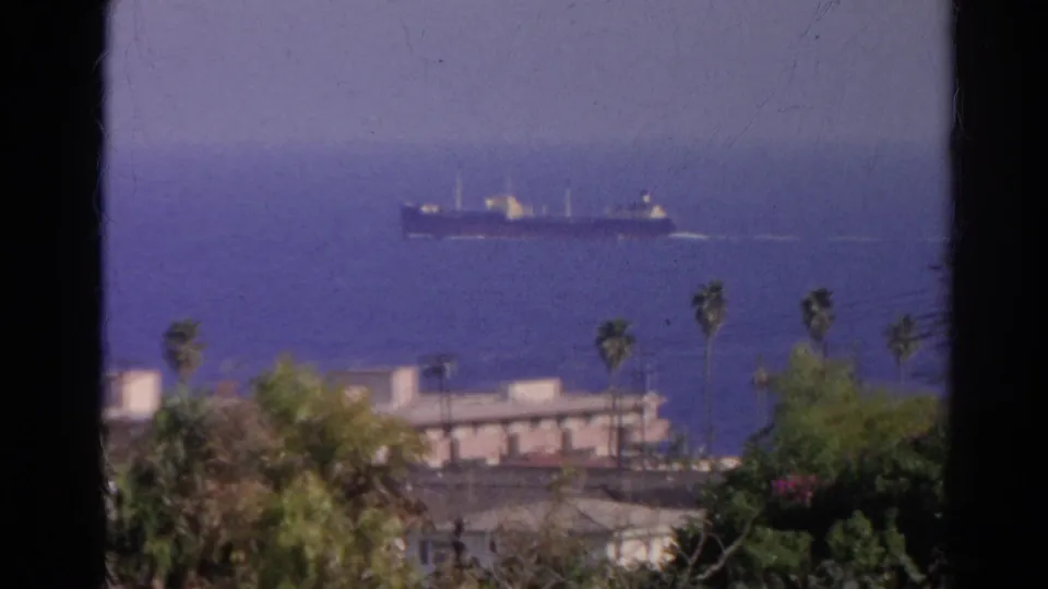 1966 Silver Lake, California 8mm view toward blue water, with a distant cargo ship beyond palms and low buildings.