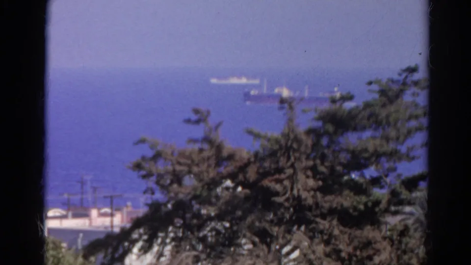 1966 8mm home-movie view of a distant cargo ship and smaller vessel beyond trees and rooftops in Silver Lake, California.