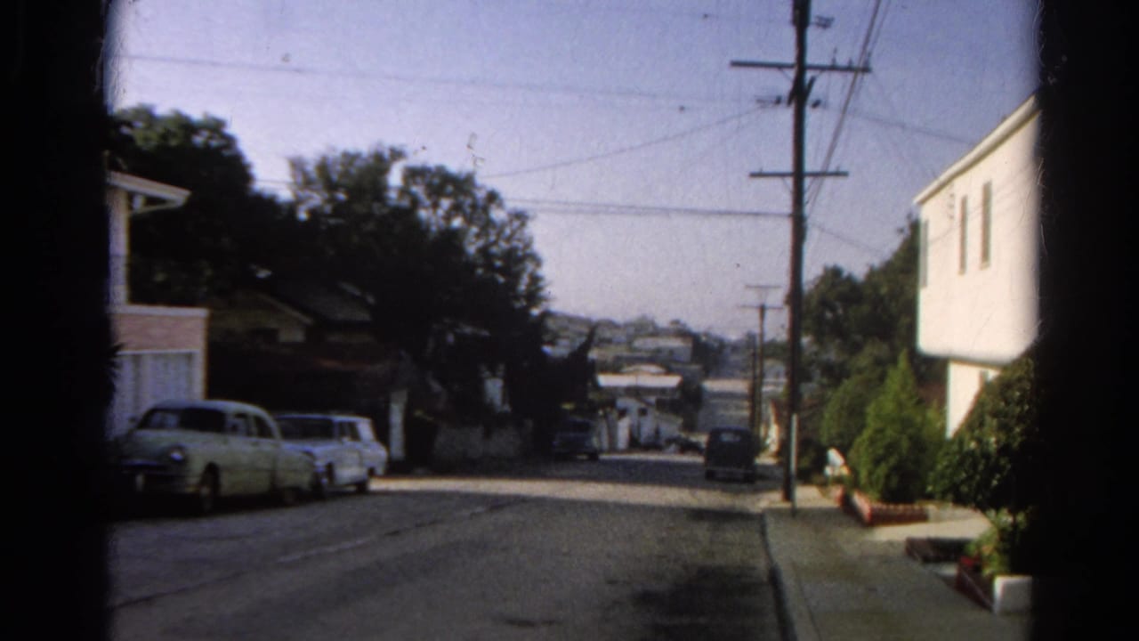 1966 Silver Lake home-movie frame looking down a residential street with parked cars, houses, trees, utility poles, and wires.