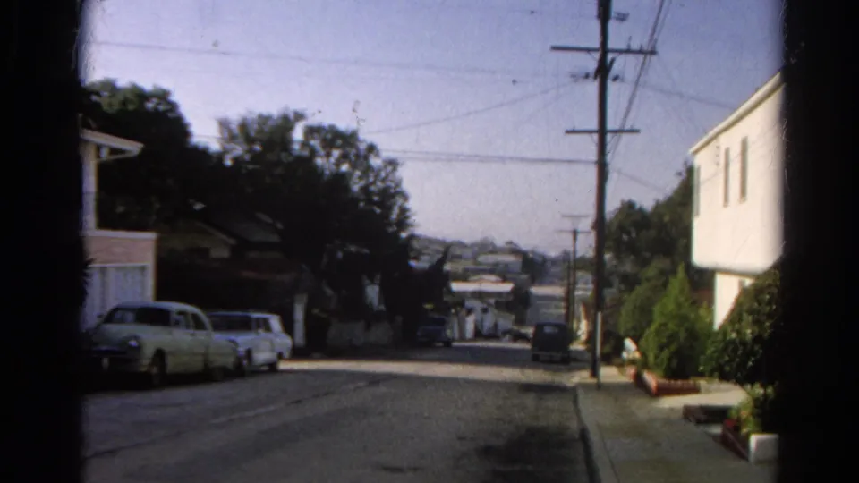 1966 Silver Lake home-movie frame looking down a residential street with parked cars, houses, trees, utility poles, and wires.