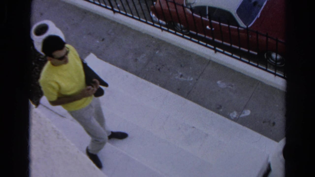 A man in a yellow shirt and light pants walks along a Silver Lake sidewalk near a railing and parked car in this 1966 home-movie frame.