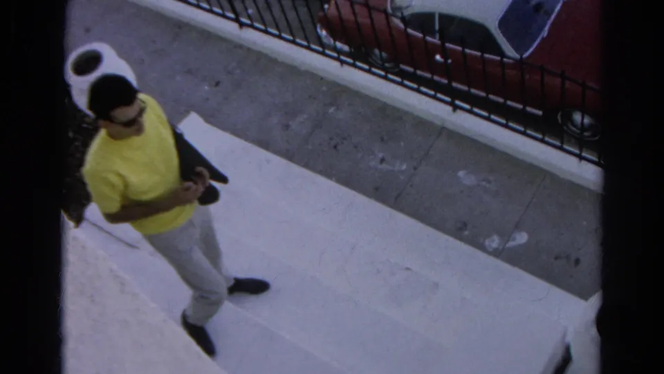 A man in a yellow shirt and light pants walks along a Silver Lake sidewalk near a railing and parked car in this 1966 home-movie frame.