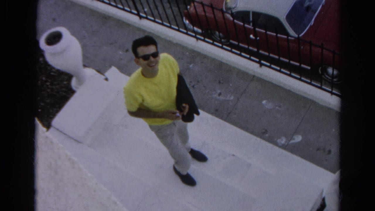 In Silver Lake home-movie footage, the young man looks up and smiles from the steps, holding a dark jacket near a sidewalk and fence.