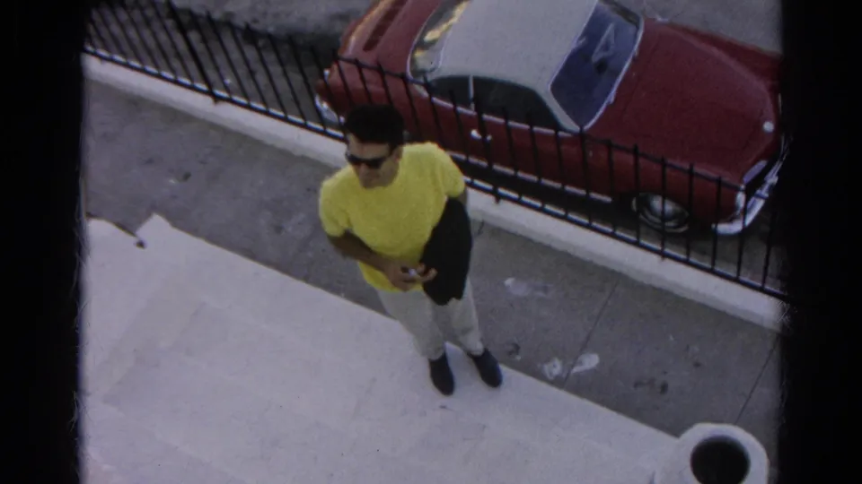 At the end of the Silver Lake clip, the man pauses near the steps as a red car, sidewalk, and black iron fence fill the background.