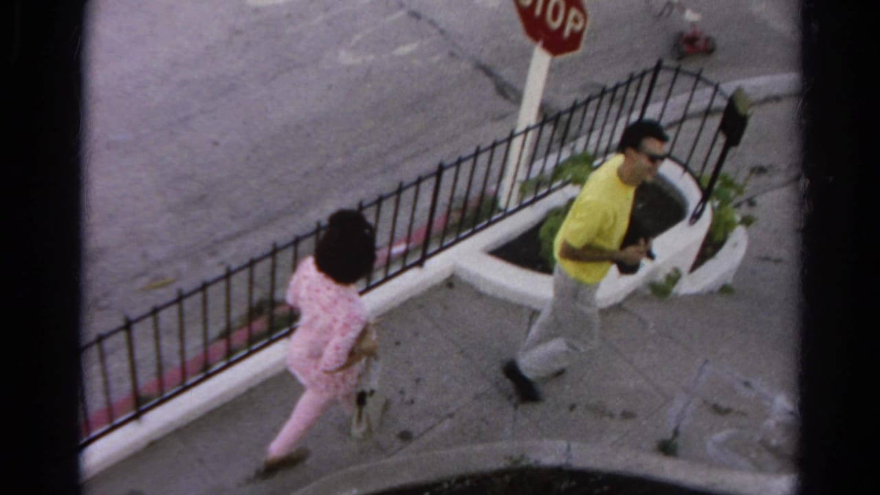 Man and woman walk toward a stop sign along a fenced corner sidewalk.