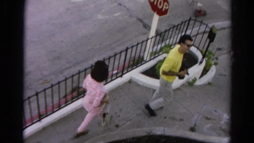 The man and woman continue along a Silver Lake sidewalk near a stop sign, low wall, planter, and black metal fence.