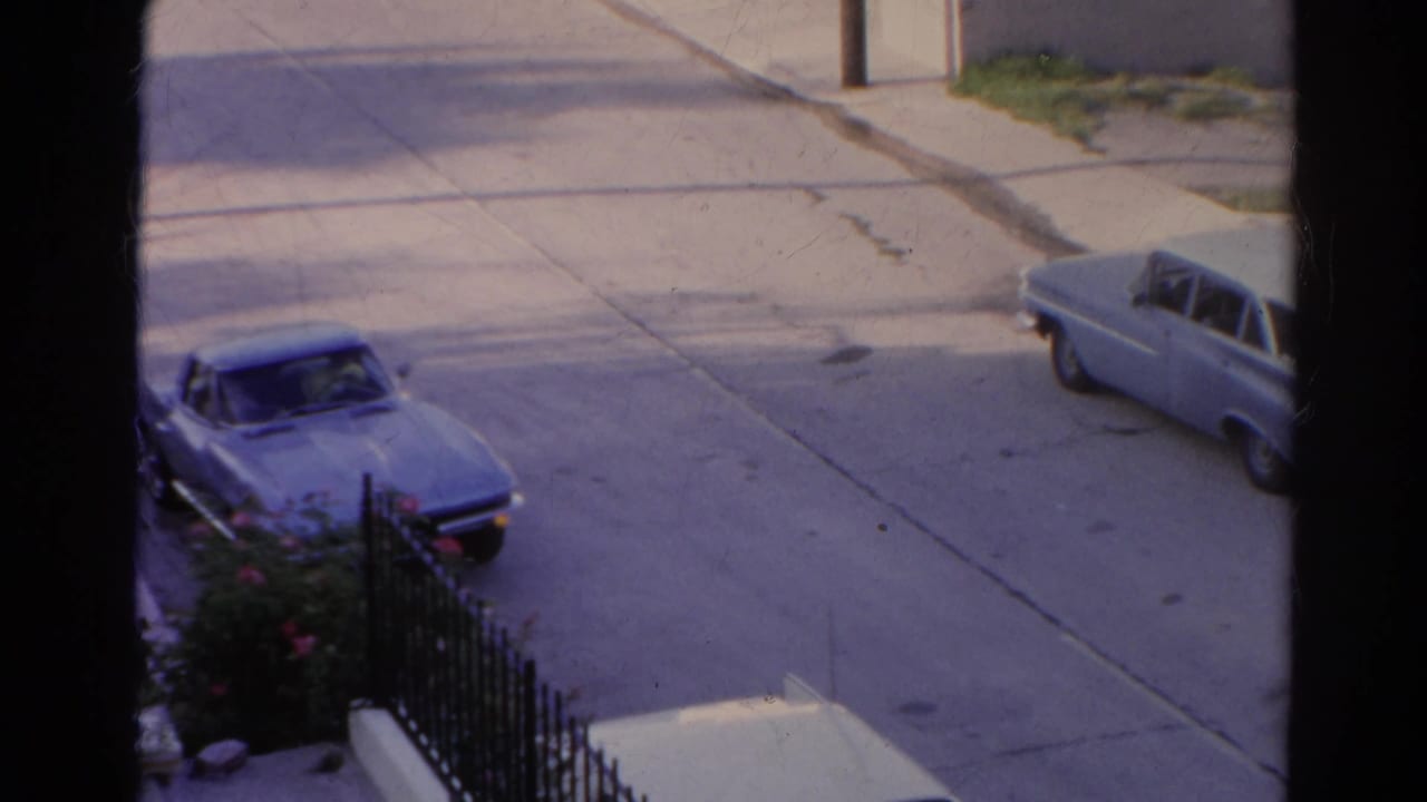 Blue convertible parked near a residential curb with another pale car across the street.
