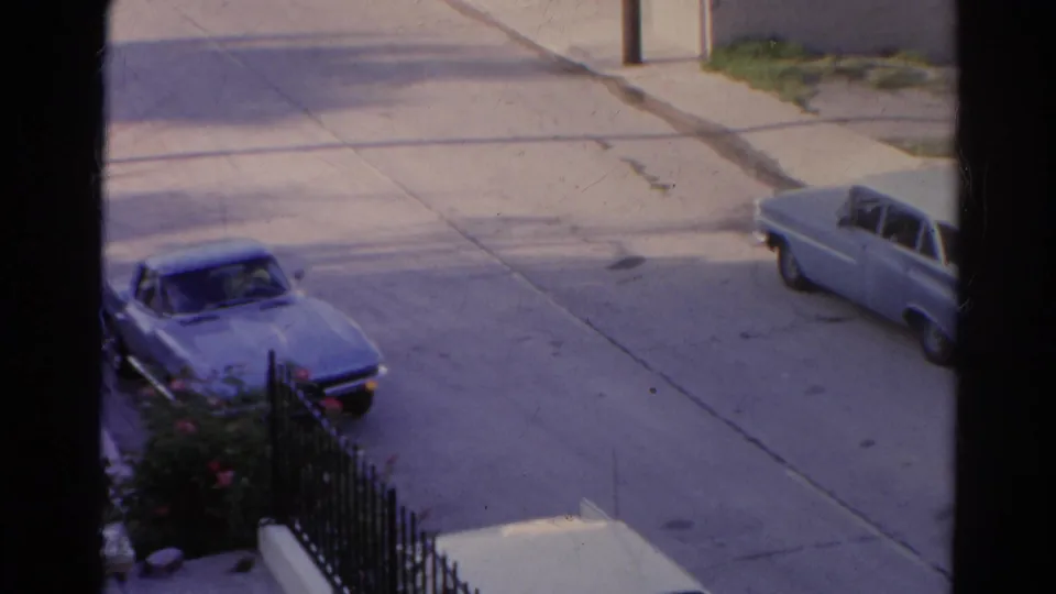 1966 Silver Lake street view through a window frame, with a blue convertible at the curb and a pale car farther along the road.