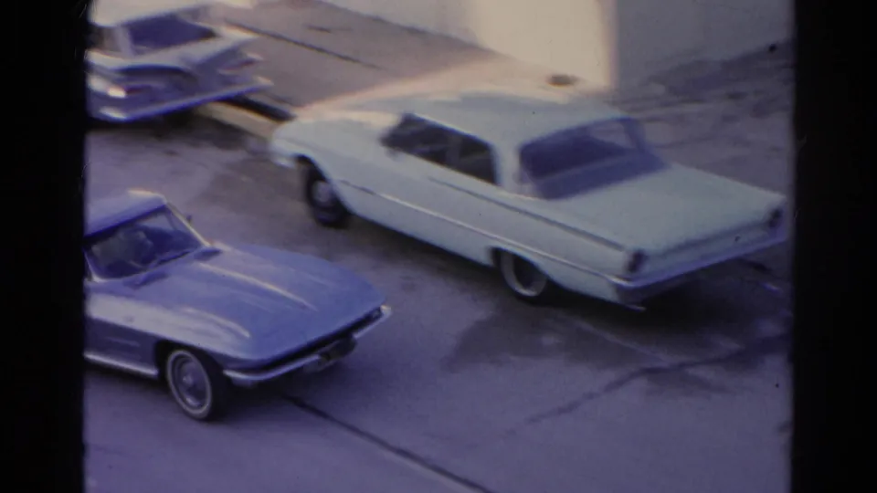 A pale 1960s car moves past the window-framed view on the Silver Lake street, with the blue convertible partly visible below.