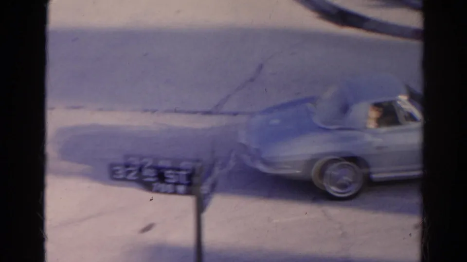 The car exits the turn beside a 32nd St street sign, with the driver area partly visible in the grainy 8mm Silver Lake footage.