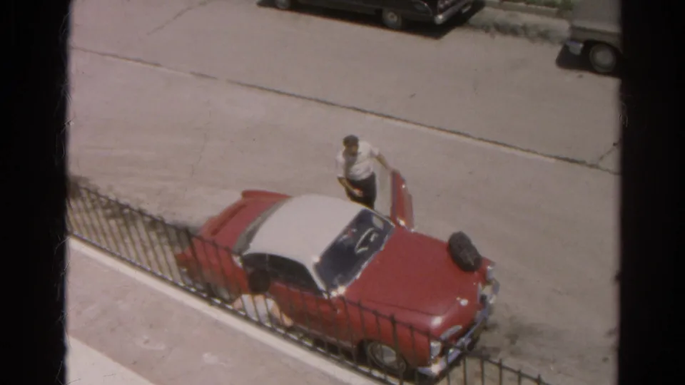 The man remains beside the open door of the two-tone car on a quiet Silver Lake street in 1966 footage.
