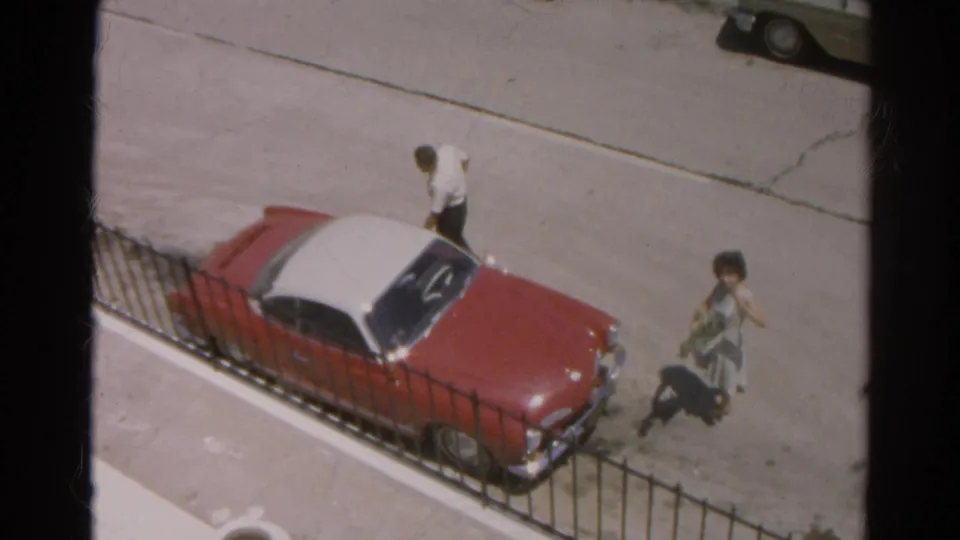 The elevated 1966 Silver Lake view shows the man by the parked red car as the woman moves along the street with a small object or package.