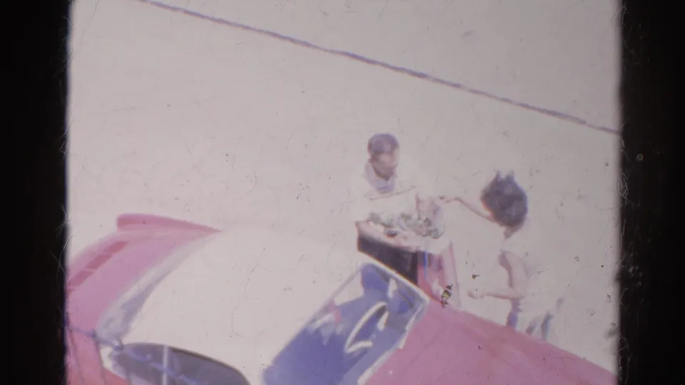 Two adults remain near the red car in Silver Lake, with the woman close to the man and the street washed by bright 8mm exposure.