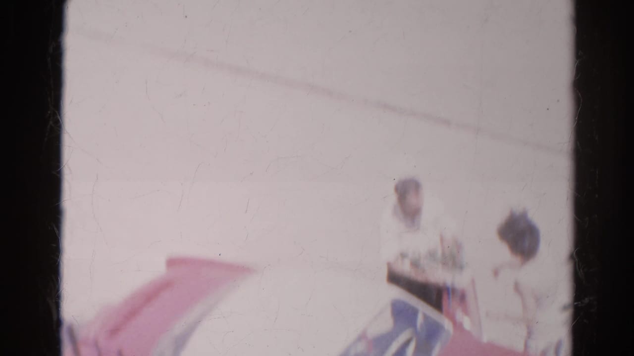 In 1966 Silver Lake footage, adults appear near a red and white car, with soft focus and visible 8mm frame edges.