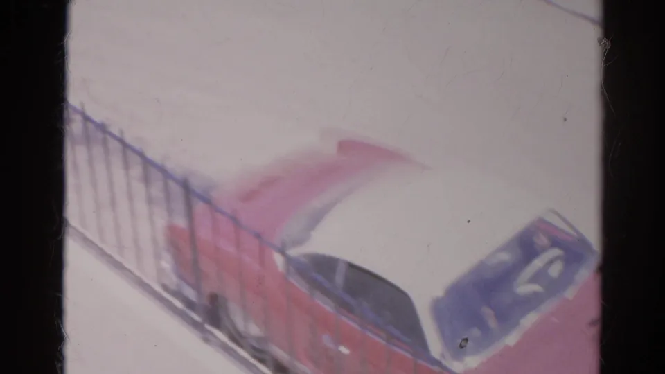 The red and white car is seen from a slightly elevated angle beside a metal fence in the 1966 Silver Lake home movie.
