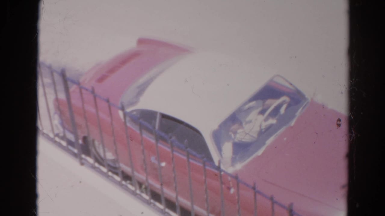 Red and white vintage car partly seen behind a black metal fence.