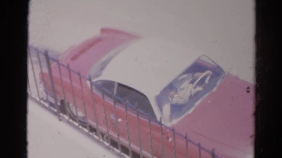 1966 Silver Lake home-movie frame showing a red and white vintage car passing behind a black metal fence.