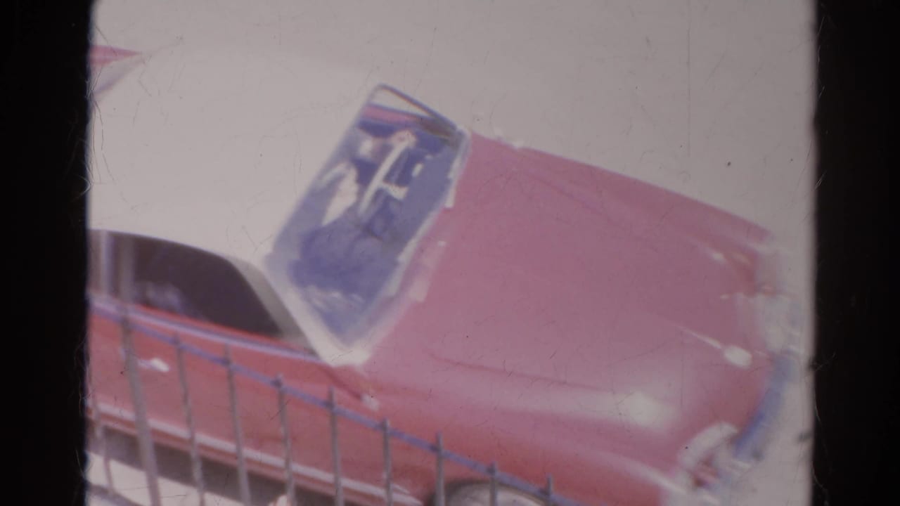 Overhead 1966 Silver Lake view of a red and white vintage car moving past a roadside fence.