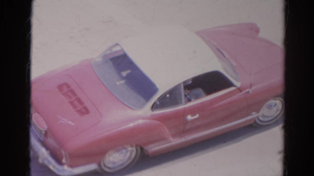 Red convertible seen from above with its rear trunk area prominent on a bright street.