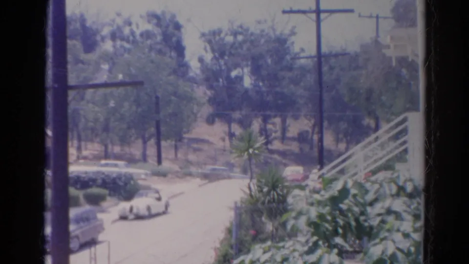 1966 Silver Lake residential view with a white convertible near parked cars, utility poles, hillside trees, shrubs, and a white stair railing.