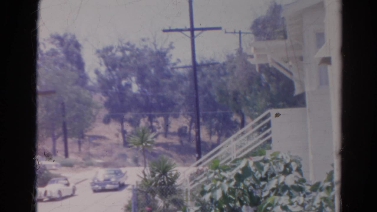 1966 Silver Lake street view with classic cars, utility poles, trees, and a pale building on the hillside.