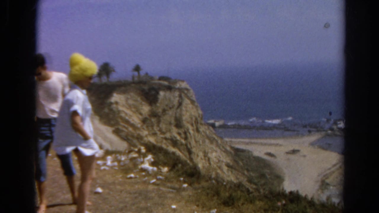 1966 8mm frame showing the woman turning beside the man on a California coastal cliff, with beach and surf in the background.