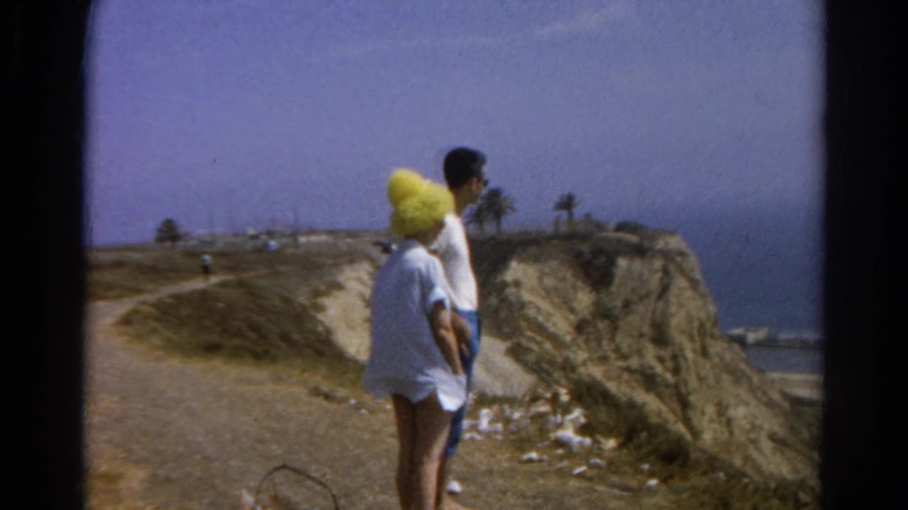 Couple viewed from behind on a dirt path near a coastal cliff and ocean.