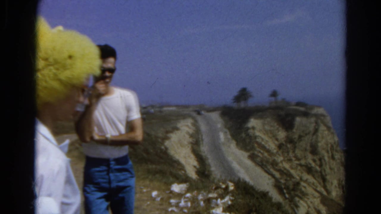 Woman in yellow hat and man in white T-shirt stand beside a cliff road.