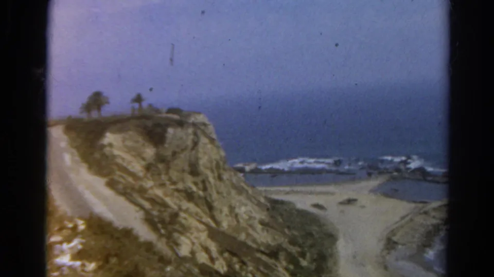 1966 8mm coastal view labeled California, showing a road along a bluff with beach and ocean beyond.