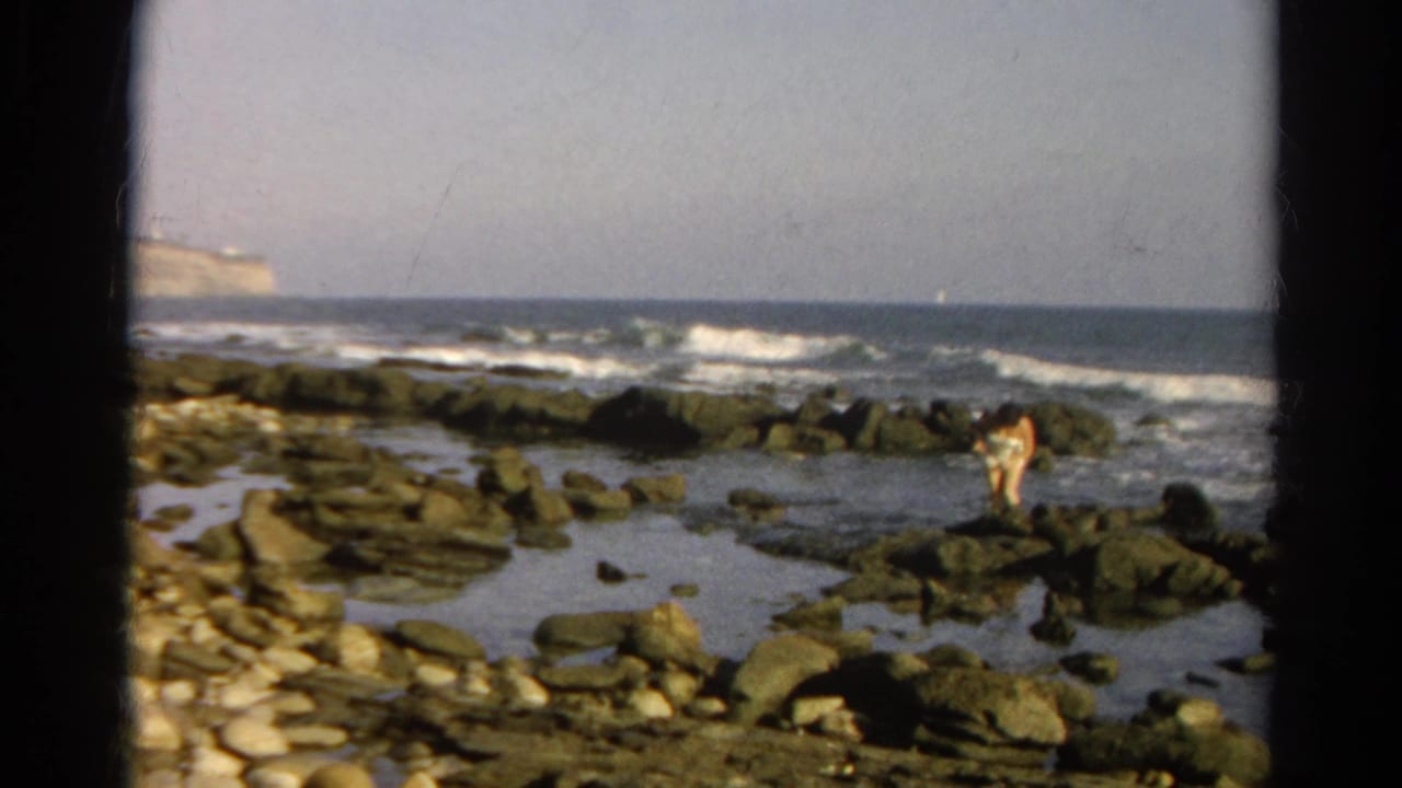 Person near the right side of a rocky shoreline with waves rolling in.