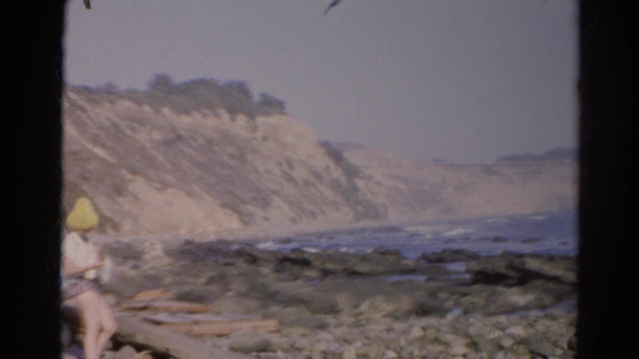 Rocky shoreline with waves and pale cliffs, plus a partial person at the far left edge.