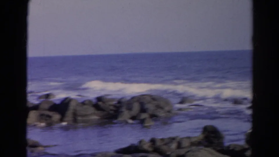1966 8mm frame identified as Silver Lake, California, showing low surf rolling toward dark rocks under a pale sky.