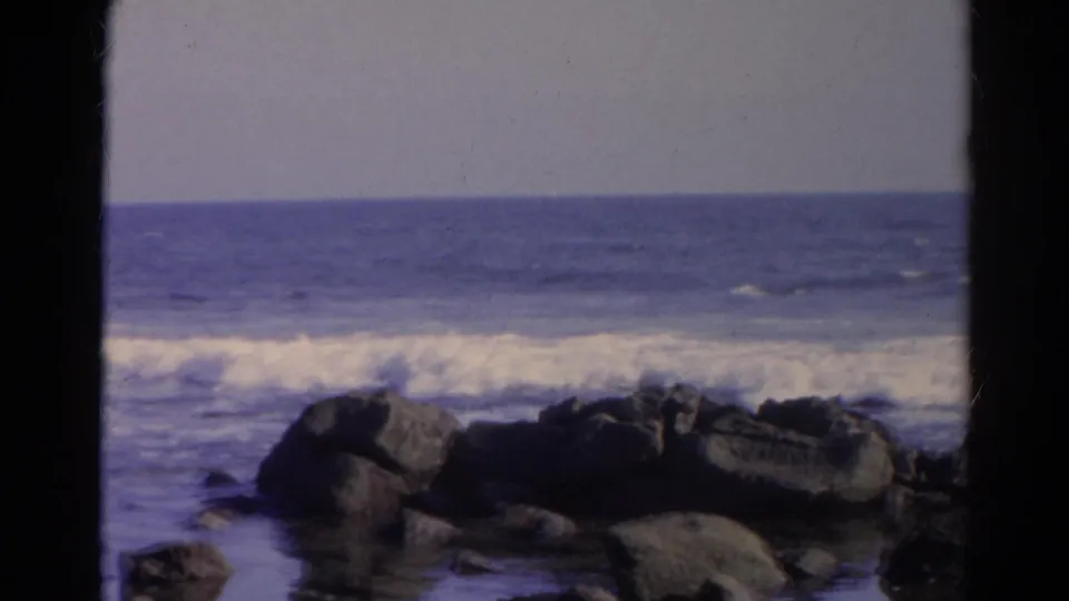 1966 8mm frame identified as Silver Lake, California, showing a band of white surf behind dark shoreline rocks.