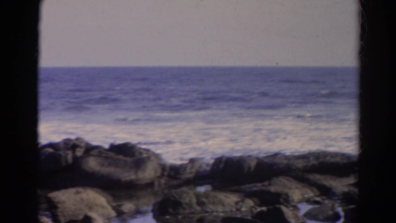 Rocky shoreline with ocean waves under a hazy sky.