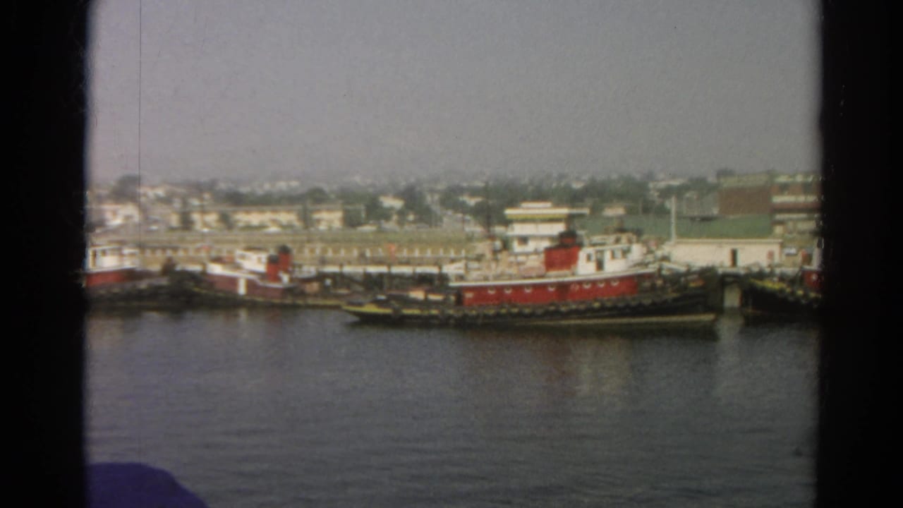 Distant red and white tugboats docked along a calm waterfront.