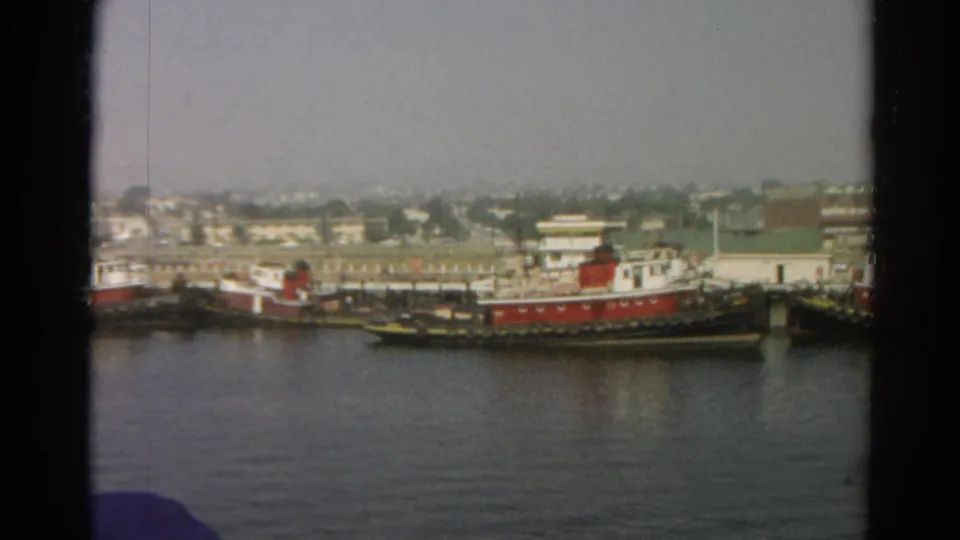 1966 8mm view of red and white tugboats docked across calm water in the listed Silver Lake, California location.