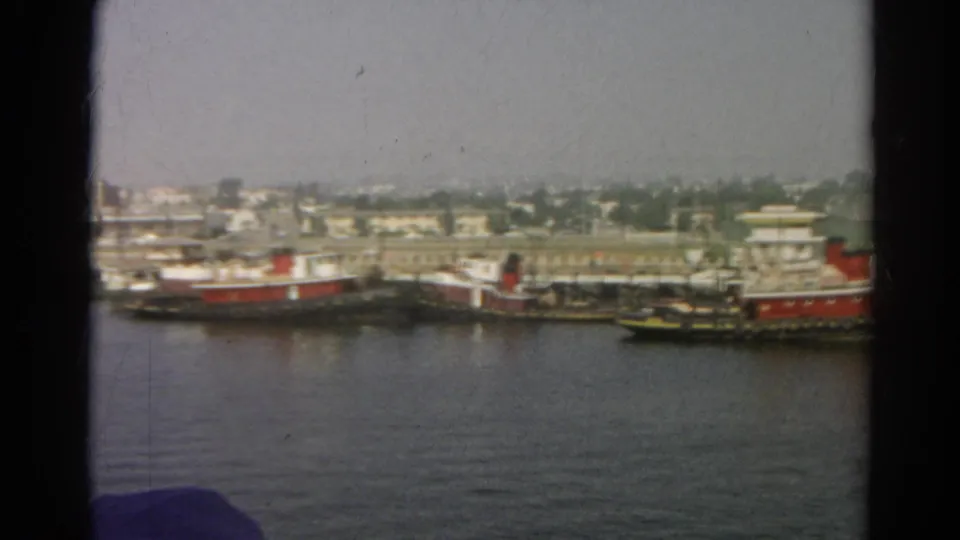Color 8mm frame from the listed 1966 California clip showing docked tugboats beside a hazy industrial shoreline.