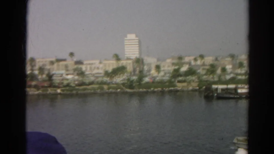 End frame of 1966 8mm California waterfront footage, showing calm water, palm-lined shore, low buildings, and a white high-rise.