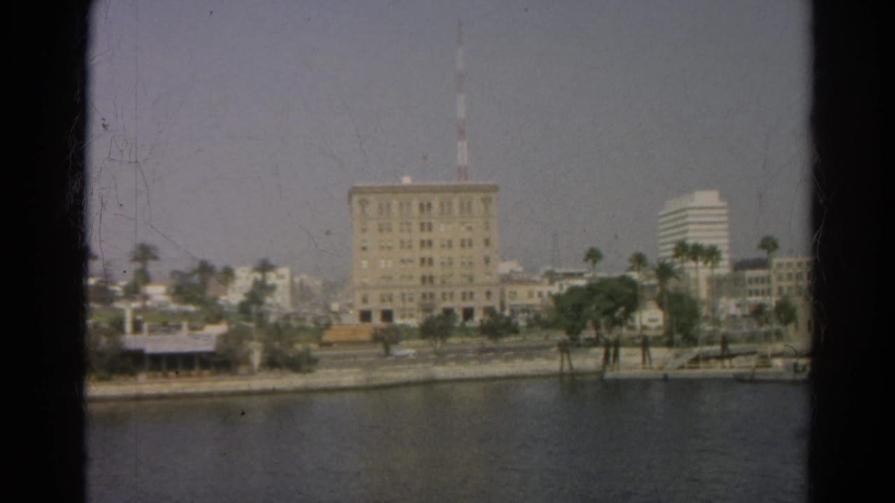 1966 Silver Lake, California home-movie frame showing a large shoreline building with an antenna beyond calm water and palms.
